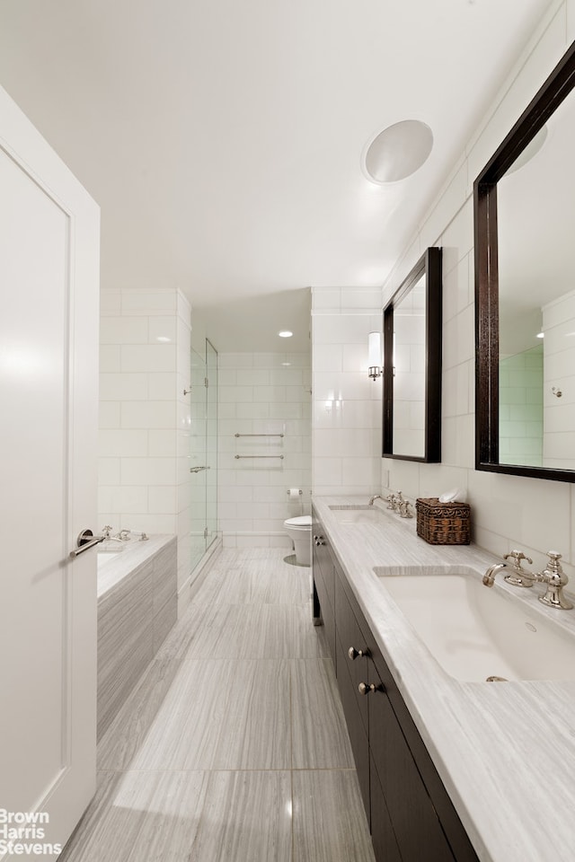 bathroom with a stall shower, a bath, toilet, tile walls, and double vanity