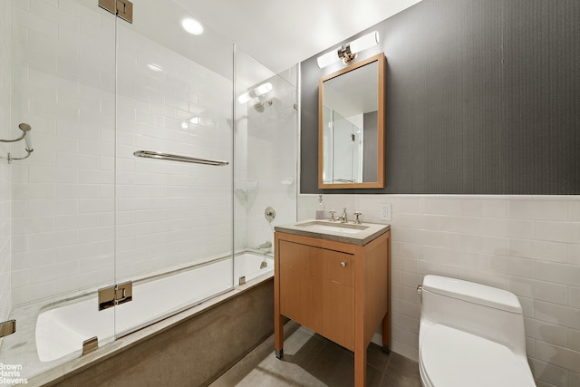 bathroom featuring a wainscoted wall, shower / bath combination with glass door, tile walls, toilet, and vanity