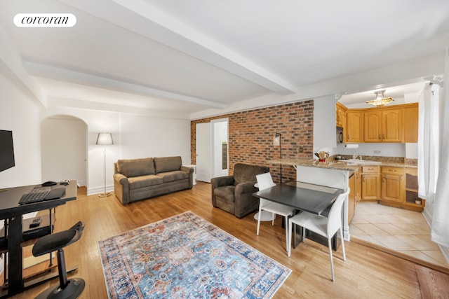 living room featuring brick wall, beam ceiling, and light hardwood / wood-style flooring