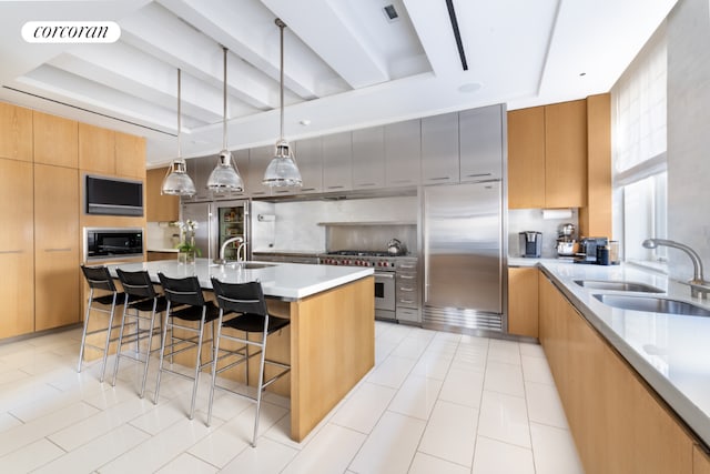 kitchen featuring a spacious island, a kitchen bar, sink, built in appliances, and hanging light fixtures