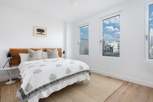 bedroom featuring baseboards, wood finished floors, and a view of city