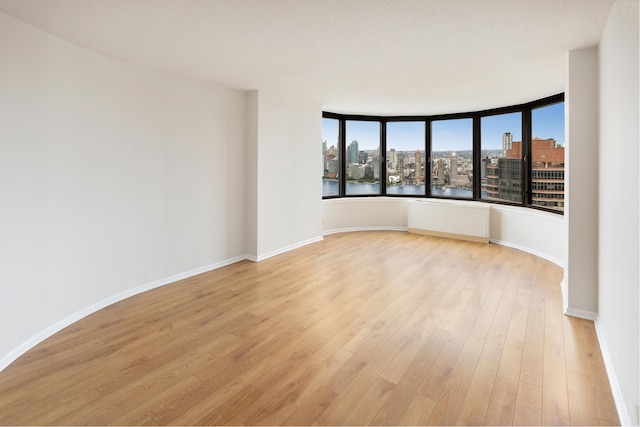 empty room with light wood finished floors, radiator, a view of city, and baseboards