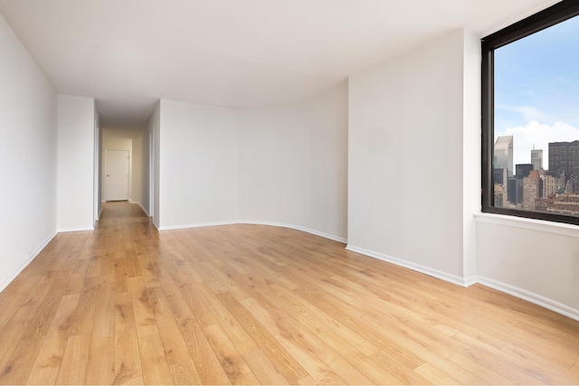 unfurnished room featuring baseboards, a view of city, and light wood finished floors