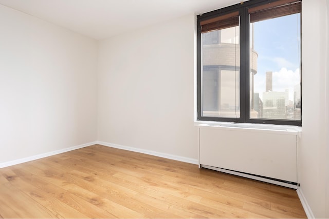 unfurnished room featuring a baseboard heating unit, baseboards, and light wood-type flooring