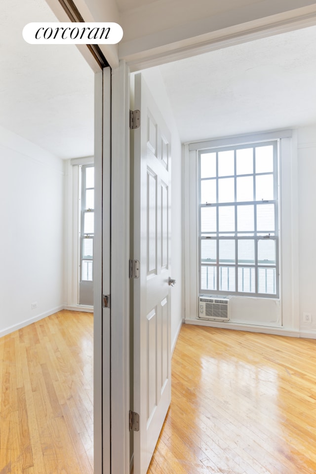 hallway featuring a wall unit AC, baseboards, and wood-type flooring