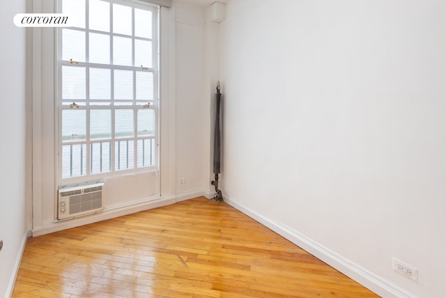 empty room with an AC wall unit, light wood-type flooring, and baseboards