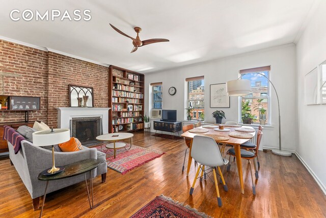 dining space featuring baseboards, a ceiling fan, ornamental molding, wood finished floors, and a fireplace