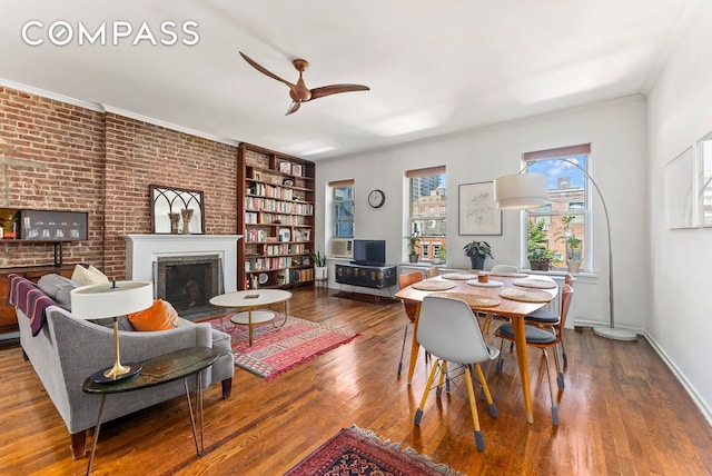 dining space featuring a ceiling fan, wood finished floors, baseboards, a fireplace, and ornamental molding