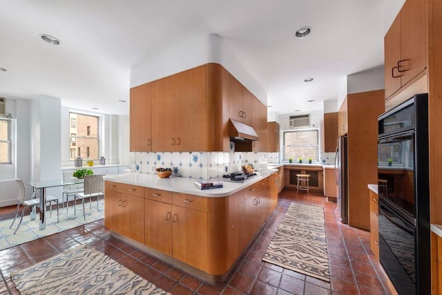 kitchen featuring light countertops, backsplash, appliances with stainless steel finishes, brown cabinetry, and under cabinet range hood