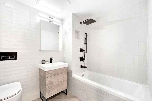 full bathroom featuring vanity, toilet, tiled shower / bath combo, and tile walls