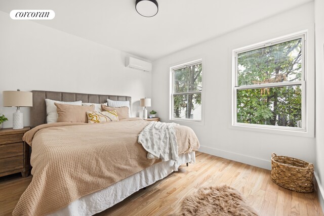 bedroom with a wall unit AC, visible vents, baseboards, and wood finished floors