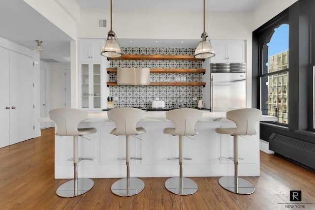 bar with hardwood / wood-style flooring, stainless steel built in refrigerator, tasteful backsplash, white cabinets, and decorative light fixtures