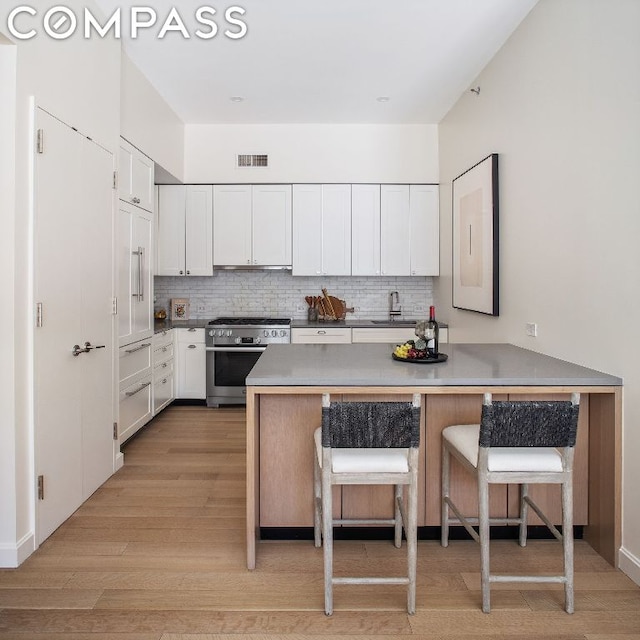 kitchen featuring white cabinetry, light hardwood / wood-style floors, a kitchen breakfast bar, stainless steel stove, and kitchen peninsula