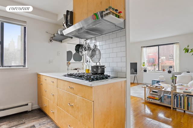 kitchen featuring a wealth of natural light, a baseboard radiator, stainless steel gas cooktop, and extractor fan