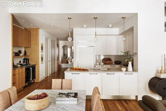 kitchen featuring decorative light fixtures, white cabinetry, sink, built in refrigerator, and dark wood-type flooring