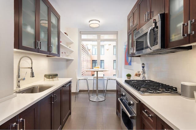 kitchen with dark tile patterned flooring, appliances with stainless steel finishes, decorative backsplash, sink, and dark brown cabinets