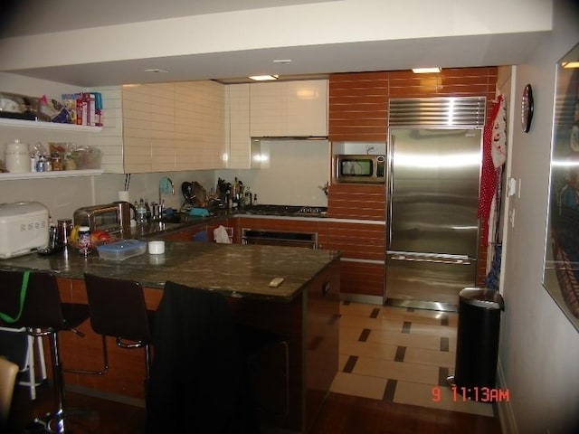 170 E End Ave Unit 2G, New York City, NY 10128 - kitchen with a kitchen breakfast bar, dark stone countertops, stainless steel appliances, a peninsula, and modern cabinets
