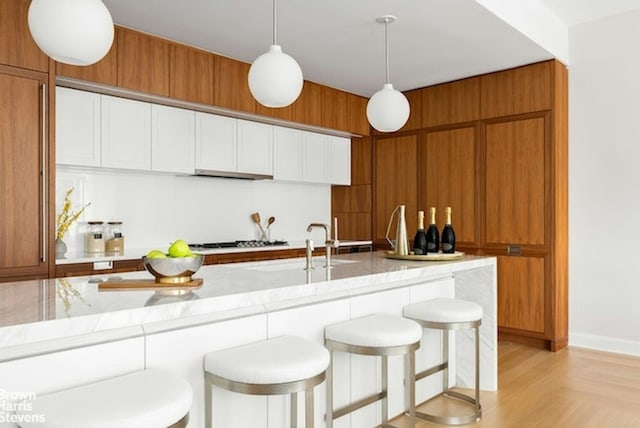 kitchen with light parquet flooring, a kitchen breakfast bar, hanging light fixtures, light stone counters, and gas cooktop