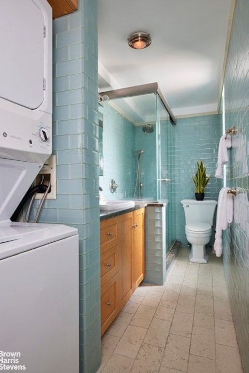 bathroom with toilet, tile walls, stacked washer / dryer, an enclosed shower, and vanity