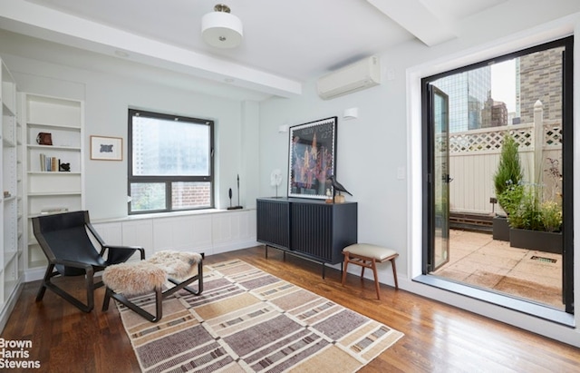 living area featuring beam ceiling, wood-type flooring, built in features, and a wall unit AC