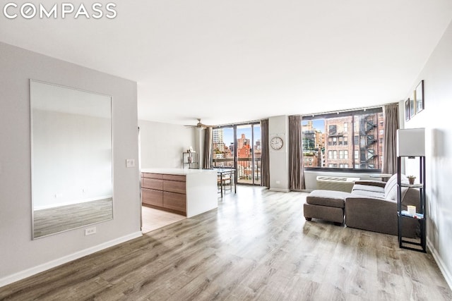 living room featuring ceiling fan, light hardwood / wood-style floors, and a wall of windows