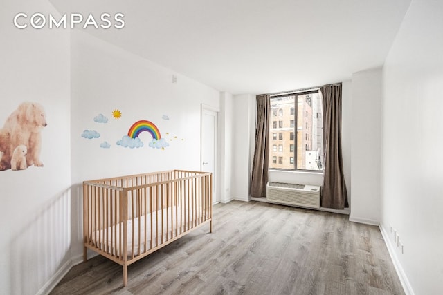 unfurnished bedroom featuring a crib, a wall unit AC, and light hardwood / wood-style floors