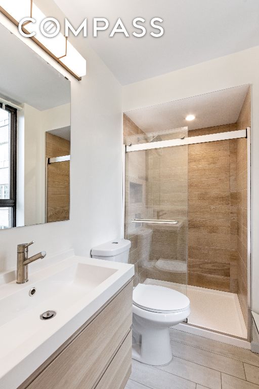 bathroom with tile patterned flooring, vanity, a shower with shower door, and toilet