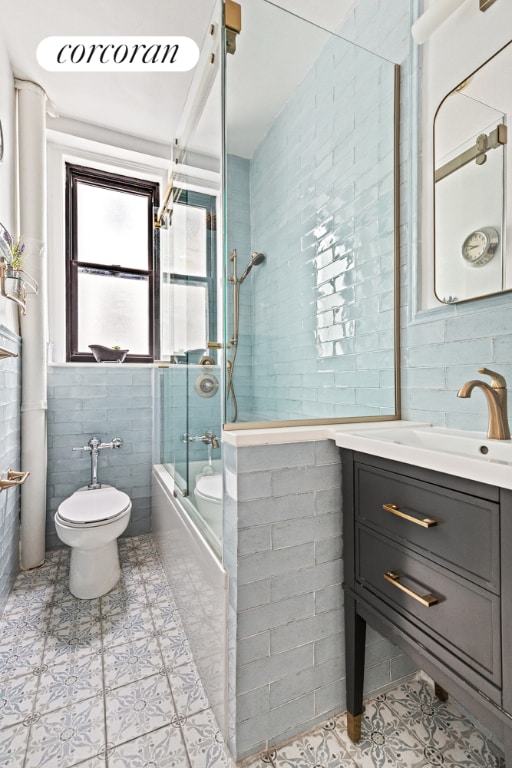 full bathroom featuring tile walls, combined bath / shower with glass door, vanity, and toilet