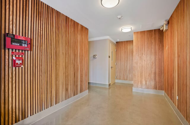 interior space featuring finished concrete flooring, crown molding, wood walls, and baseboards