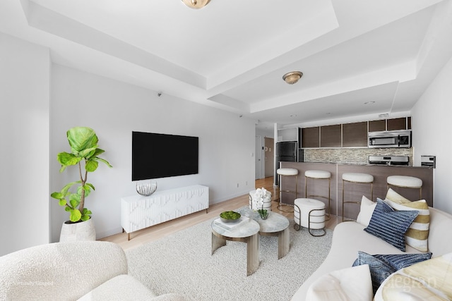 living room featuring a raised ceiling and light wood-type flooring