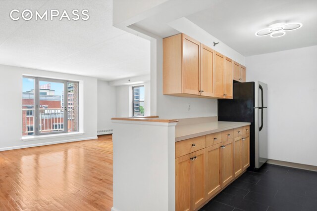 kitchen with radiator, light brown cabinetry, kitchen peninsula, and stainless steel refrigerator