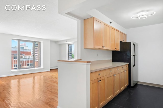 kitchen with dark wood-type flooring, light brown cabinetry, stainless steel refrigerator, radiator, and kitchen peninsula