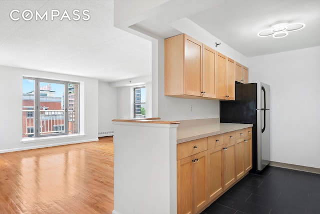 kitchen featuring light brown cabinets, a baseboard heating unit, light countertops, freestanding refrigerator, and dark wood-style floors