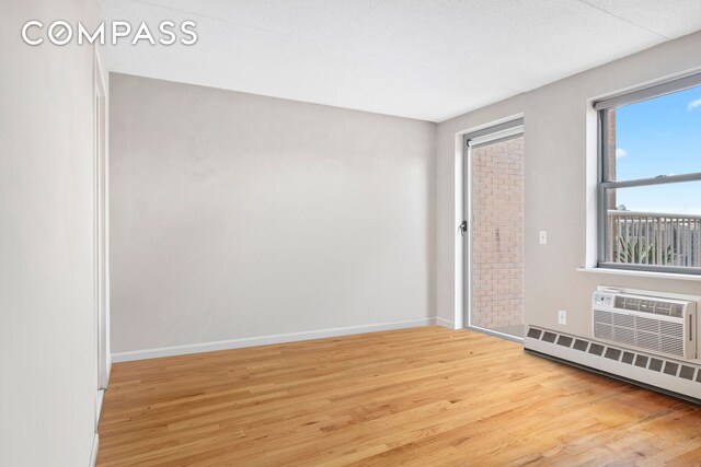 unfurnished room featuring wood-type flooring, a wall unit AC, and a baseboard heating unit