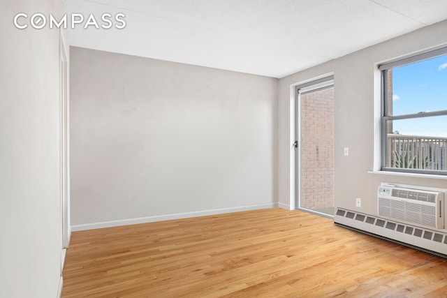 spare room with a baseboard radiator, baseboards, wood finished floors, and a wall mounted air conditioner