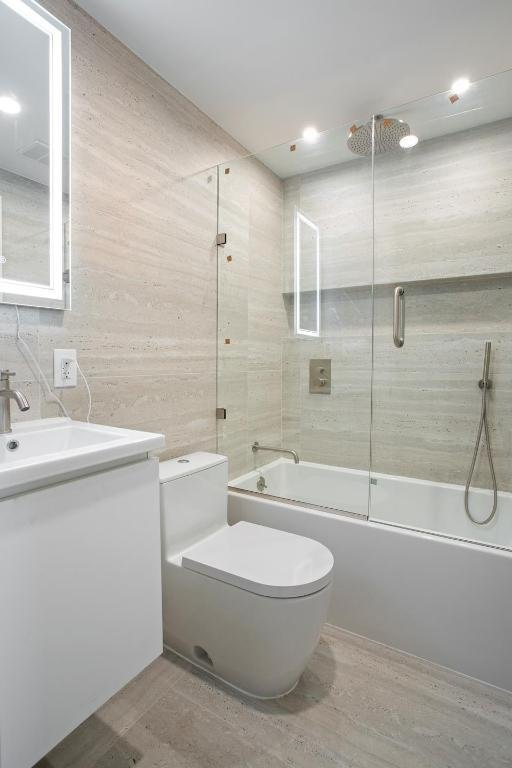 full bathroom featuring toilet, bath / shower combo with glass door, tile walls, and vanity