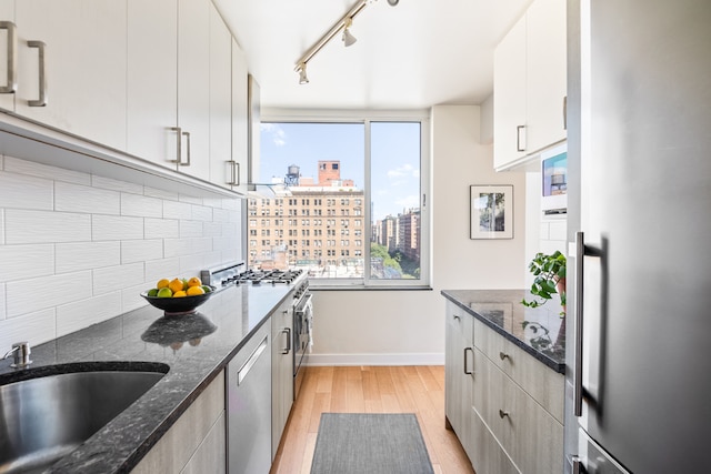 kitchen with white cabinetry, stainless steel appliances, dark stone counters, decorative backsplash, and light hardwood / wood-style flooring