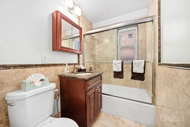 bathroom featuring toilet, a wainscoted wall, vanity, tile walls, and combined bath / shower with glass door