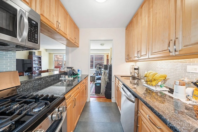 kitchen with appliances with stainless steel finishes, backsplash, light brown cabinetry, dark stone counters, and sink