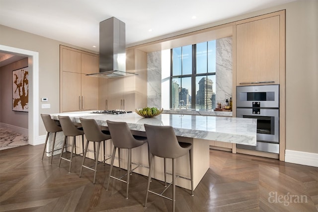 kitchen featuring a breakfast bar, light stone counters, light brown cabinets, dark parquet floors, and island exhaust hood