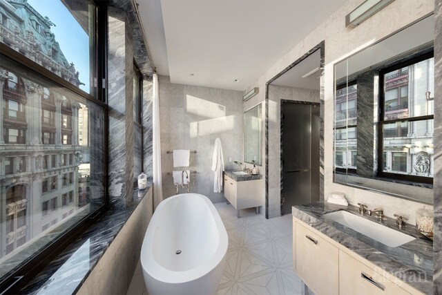 bathroom featuring vanity, a bath, and tile walls