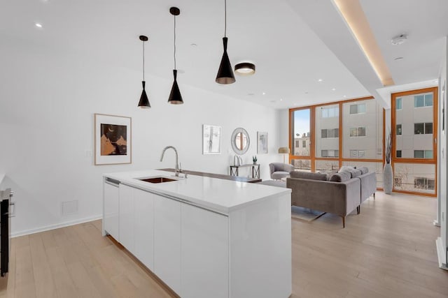 kitchen featuring sink, hanging light fixtures, an island with sink, light hardwood / wood-style floors, and white cabinets