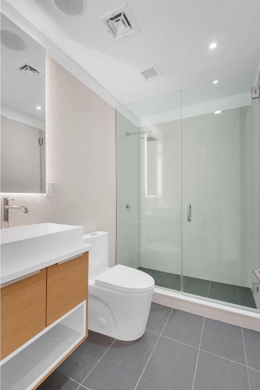 bathroom with tile patterned flooring, vanity, walk in shower, and toilet