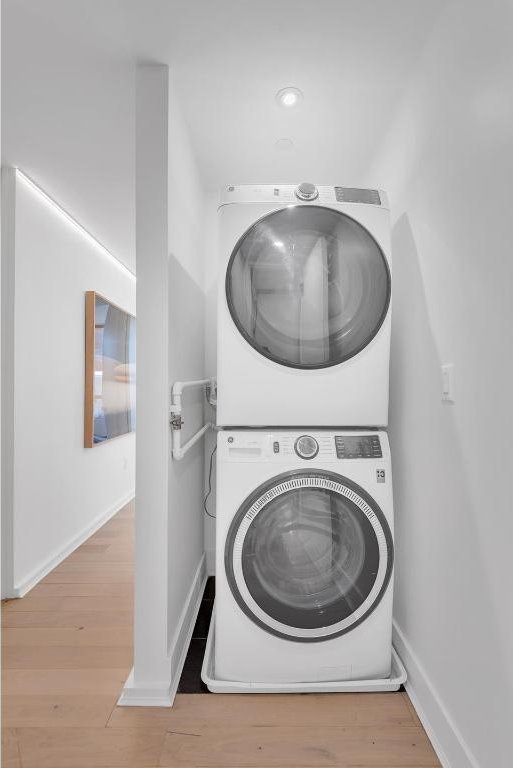 clothes washing area with light wood-type flooring and stacked washer / dryer