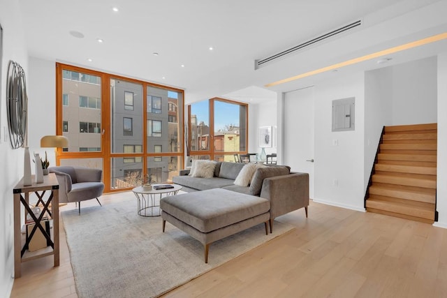 living room featuring floor to ceiling windows, stairs, light wood-type flooring, electric panel, and recessed lighting