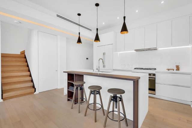 kitchen featuring white cabinetry, a kitchen island with sink, sink, and decorative light fixtures