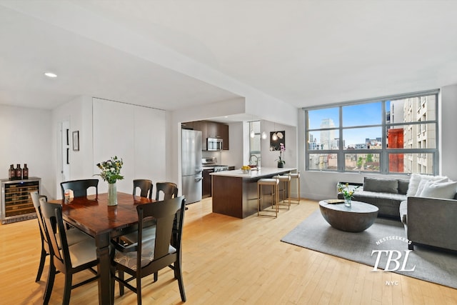 dining space with wine cooler, sink, and light hardwood / wood-style flooring