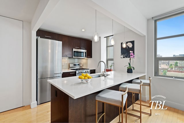 kitchen with sink, dark brown cabinets, hanging light fixtures, appliances with stainless steel finishes, and kitchen peninsula