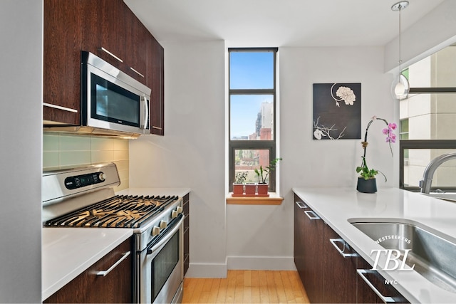 kitchen with appliances with stainless steel finishes, pendant lighting, tasteful backsplash, sink, and dark brown cabinetry