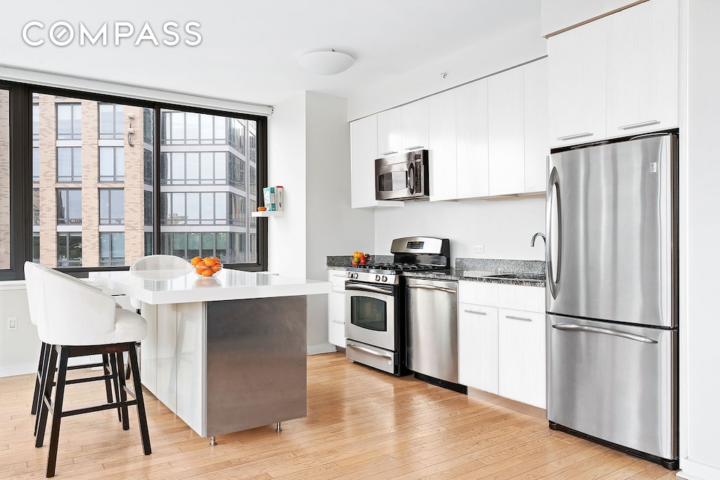 kitchen with light wood-type flooring, a kitchen bar, a sink, white cabinetry, and appliances with stainless steel finishes